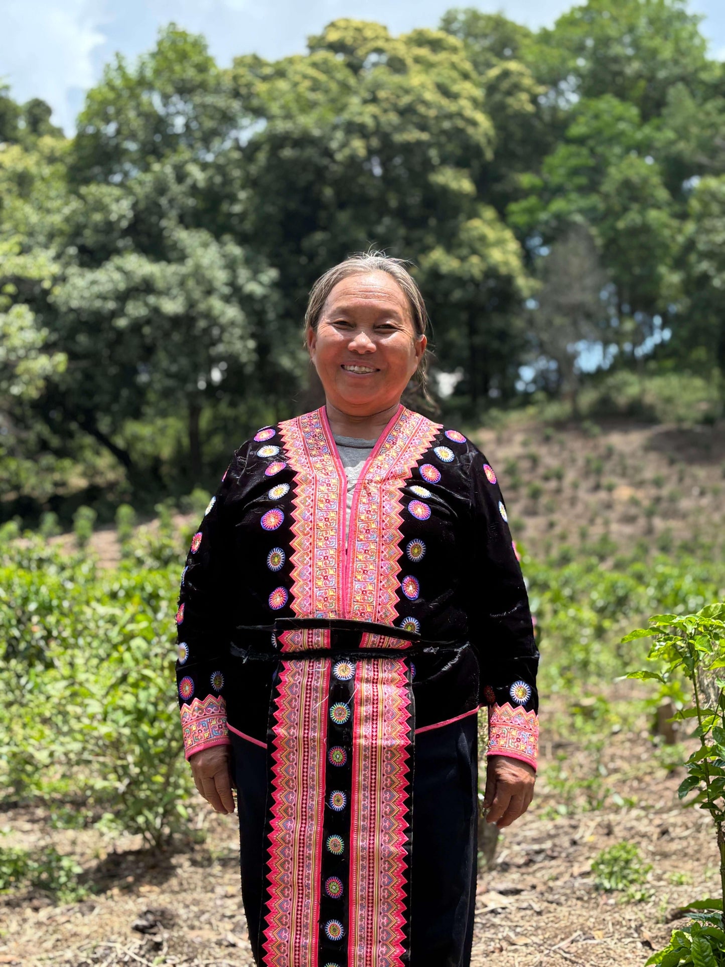 Woman in traditional attire standing in a lush green coffee field, showcasing cultural heritage and connection to agriculture.