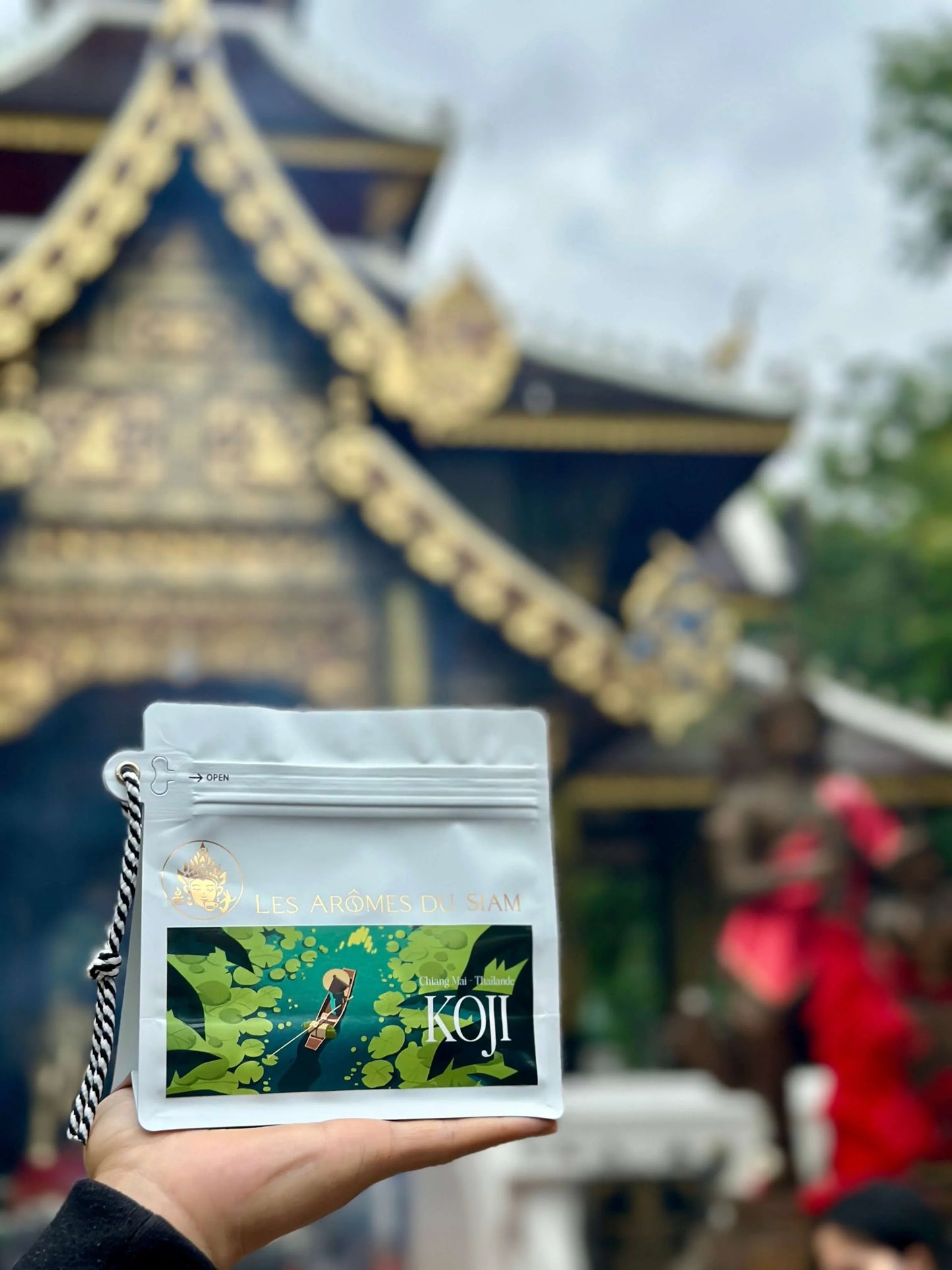 Package of Koji coffee in front of a traditional Thai temple, showcasing the unique blend influences.